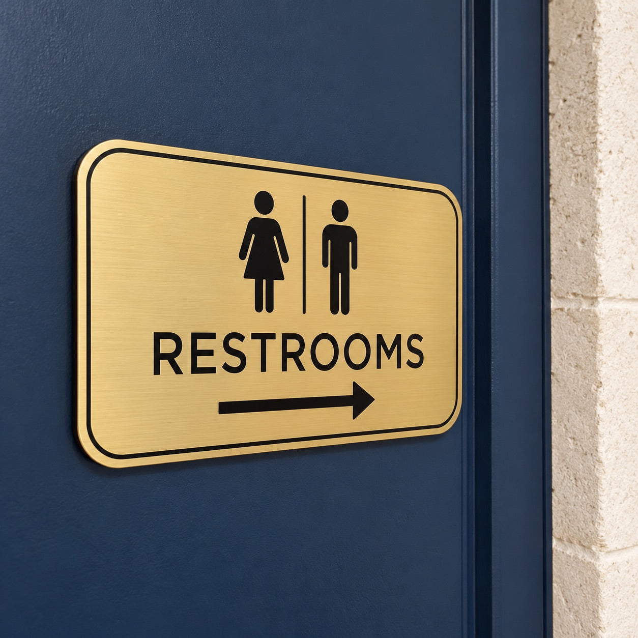 Brushed gold restroom sign with an arrow on a navy door